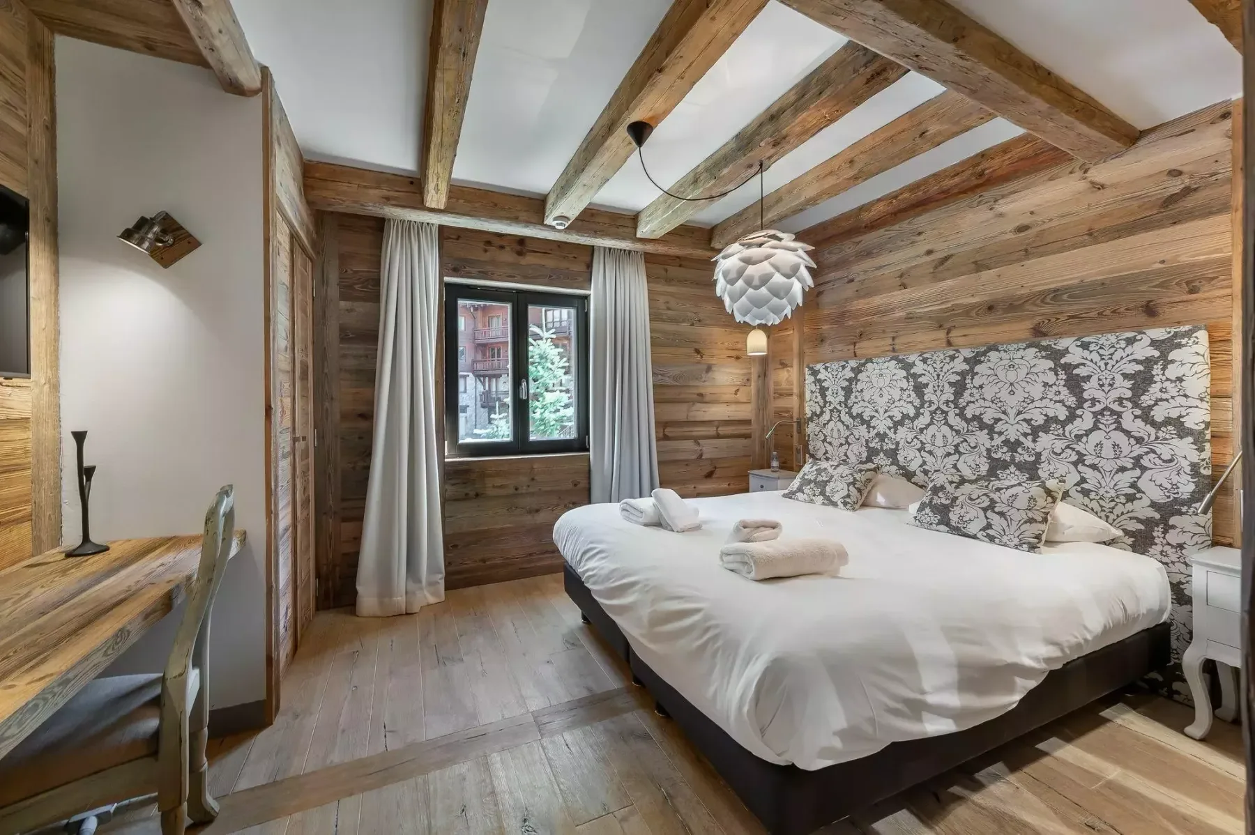 Dormitorio con una cama grande, paredes revestidas de madera y vigas vistas en el techo.