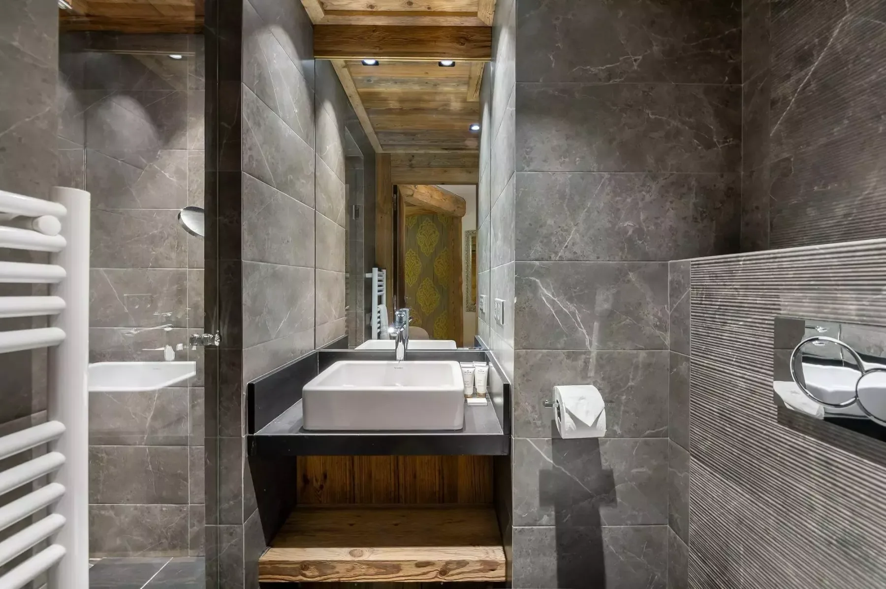 Un baño revestido de azulejos con lavabo y toallero calefactable blanco.