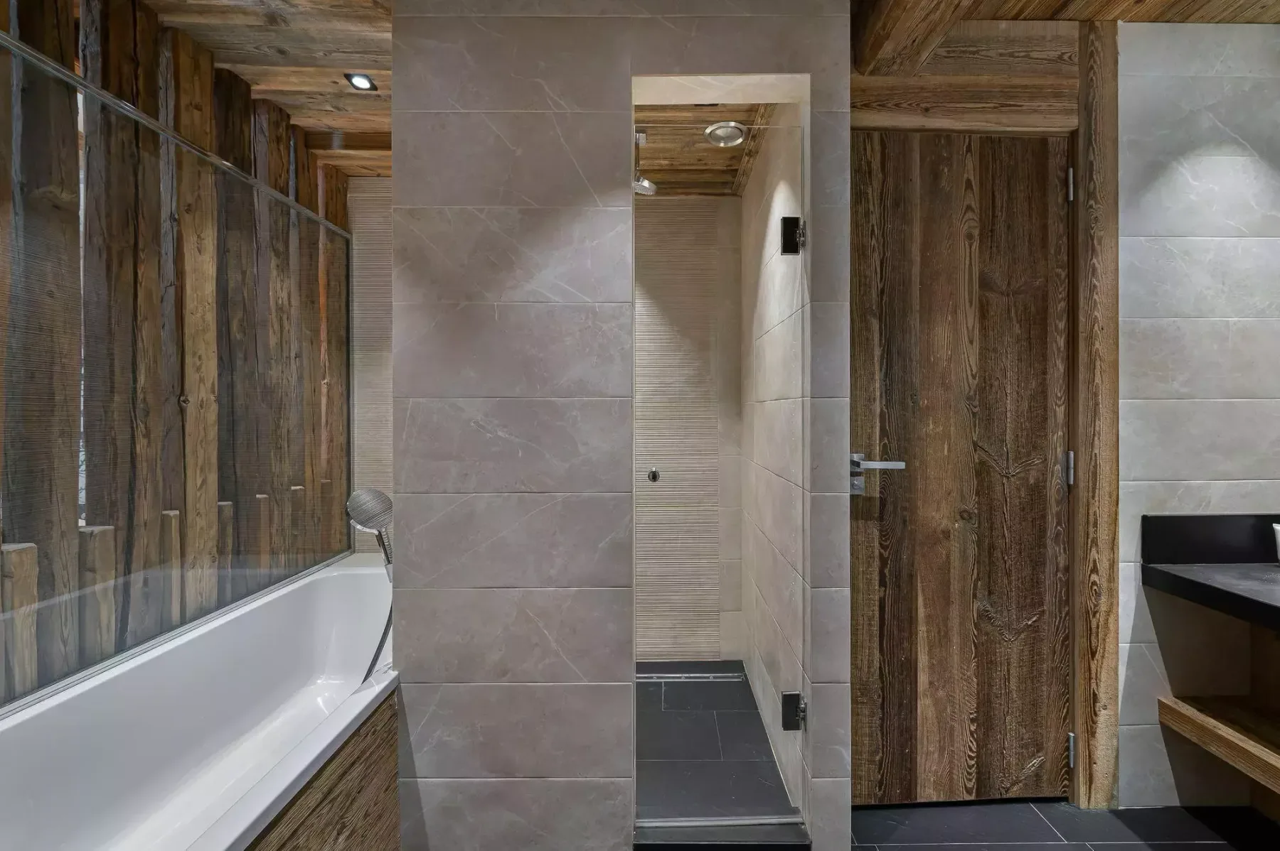 Un baño con bañera, zona de ducha alicatada y acabados de madera oscura.