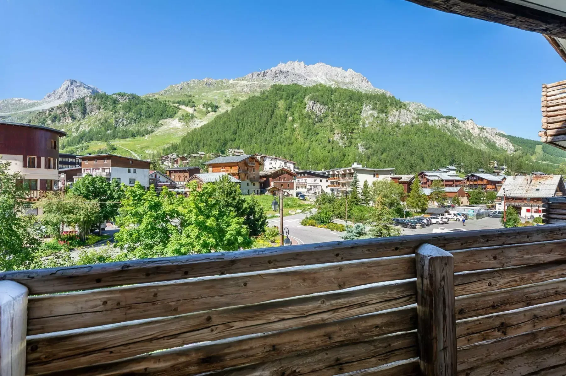Un balcón de madera da a un pueblo de montaña bajo un cielo azul despejado.