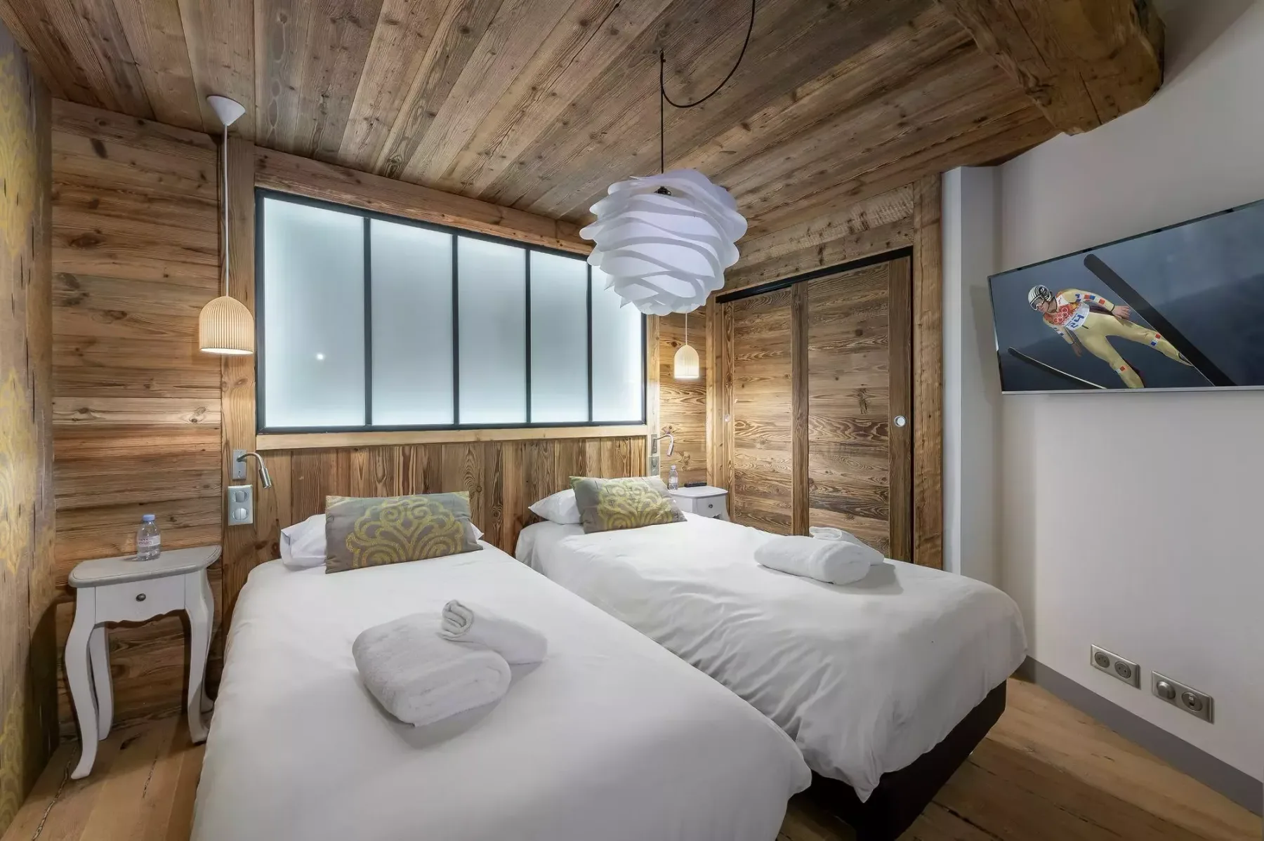 Un dormitorio revestido de madera con dos camas y una gran ventana translúcida.