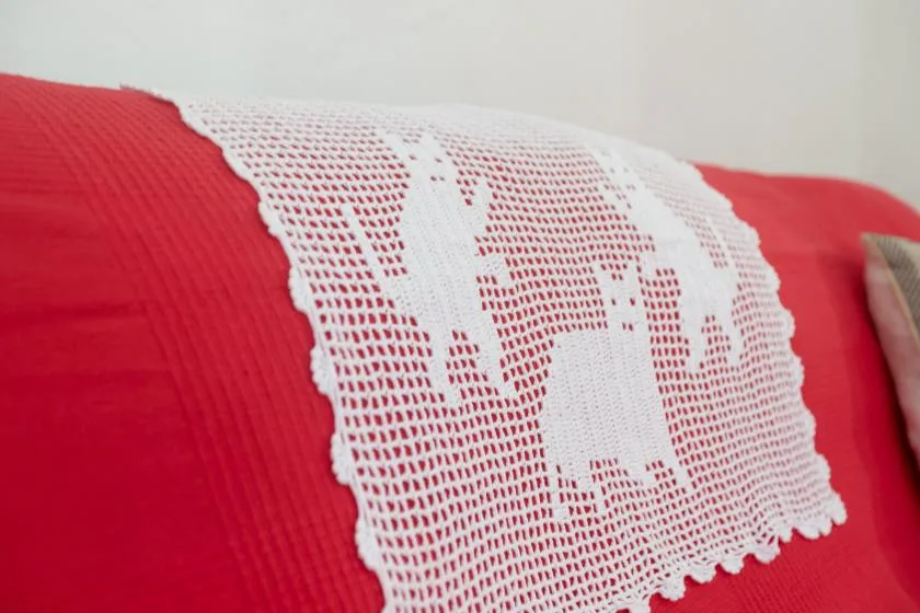 A red bedspread is draped with a white crocheted runner.