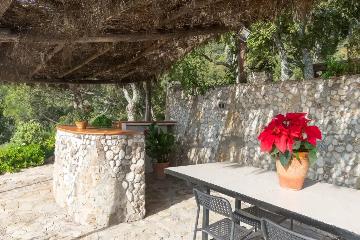 An outdoor dining area sits beneath a wooden pergola beside a stone counter.