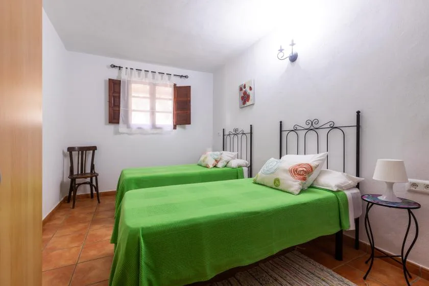 A bedroom with green-covered beds and a small wooden chair.
