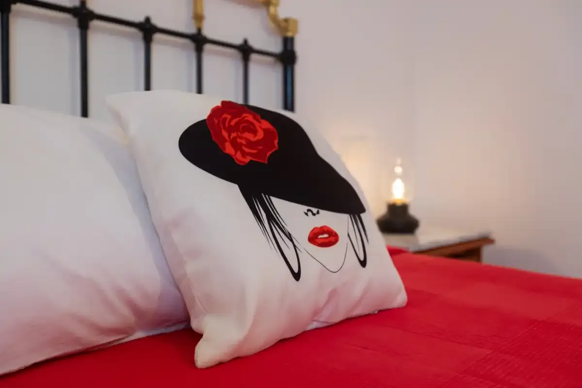 A bedroom with red bedding and a decorative pillow featuring a face.
