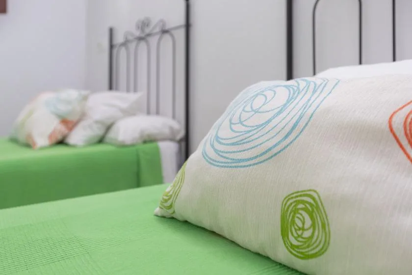 A bedroom with green bedding and patterned pillows on metal beds.