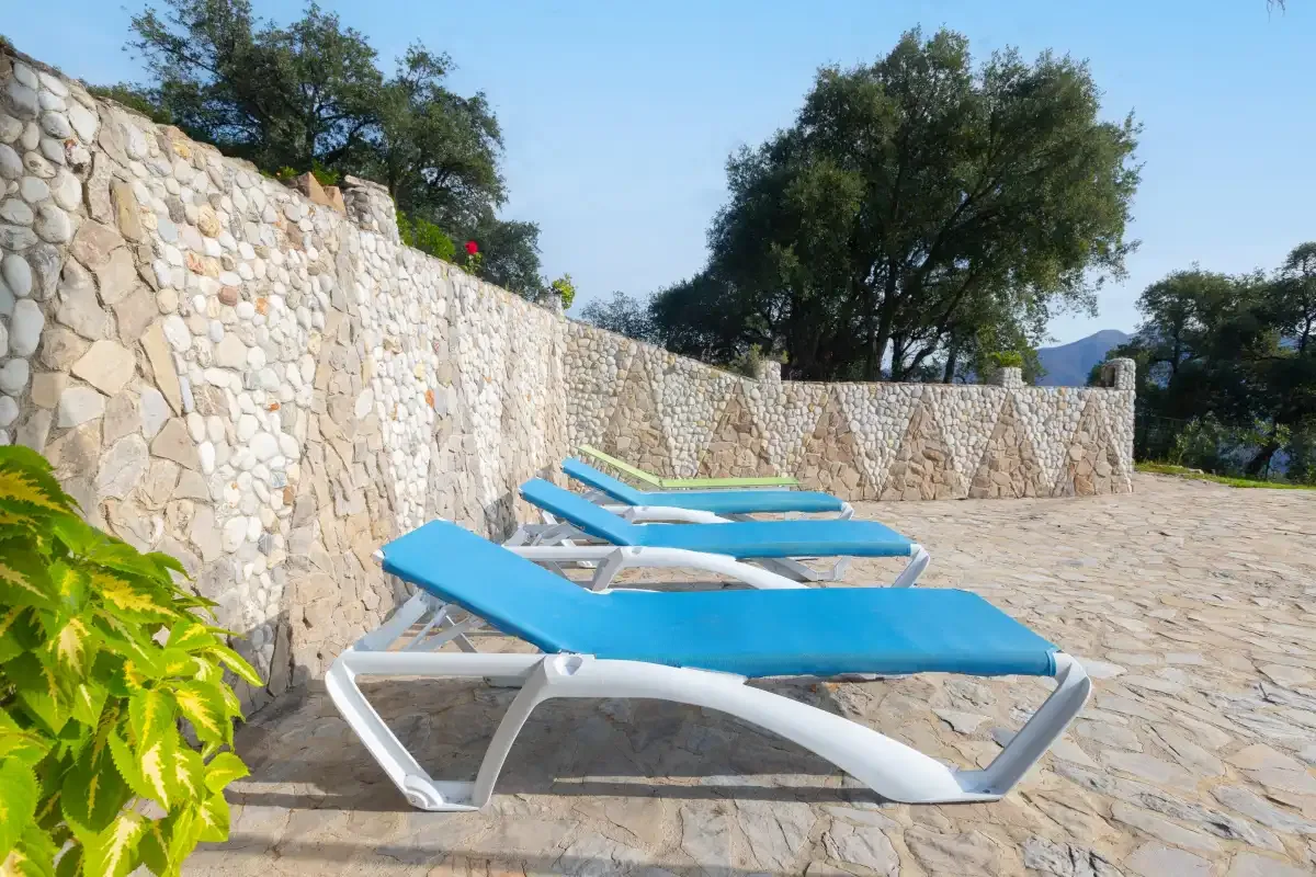 Outdoor poolside area with blue sun loungers on a stone terrace.