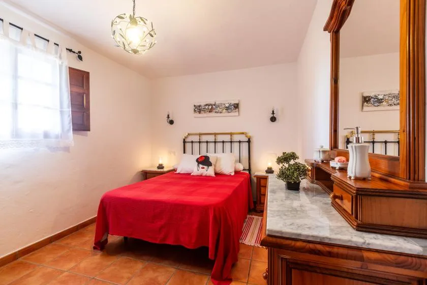 A bedroom with a red bedspread, bedside tables, and a large wooden dresser.