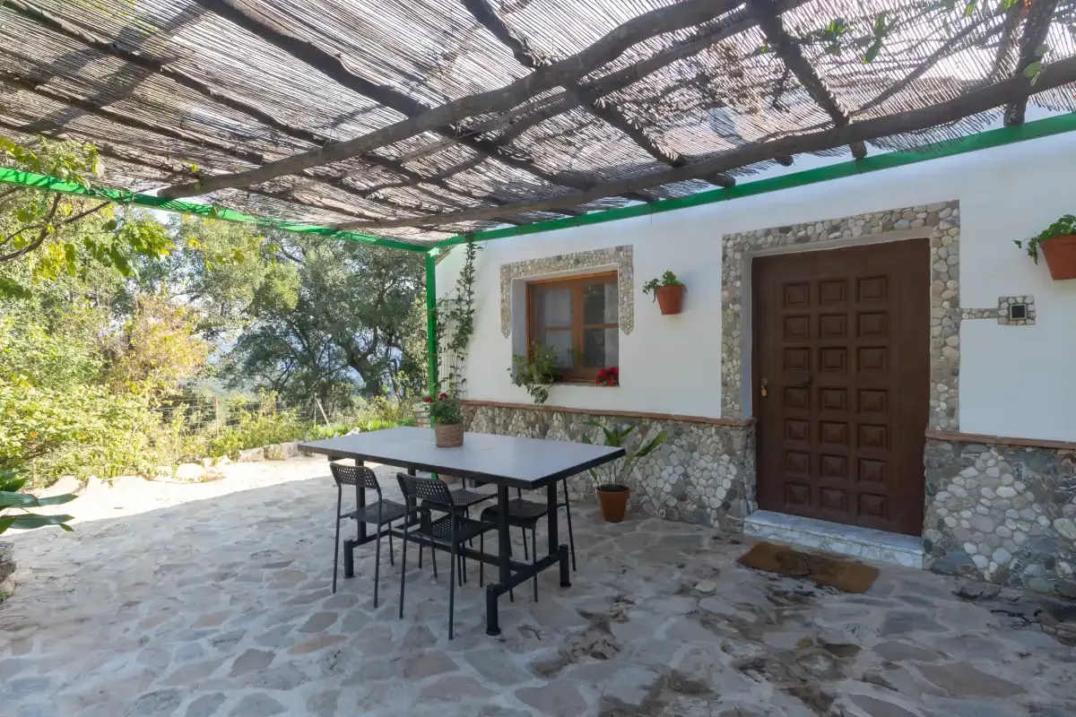 A shaded outdoor patio with a table and seating beside a white building.