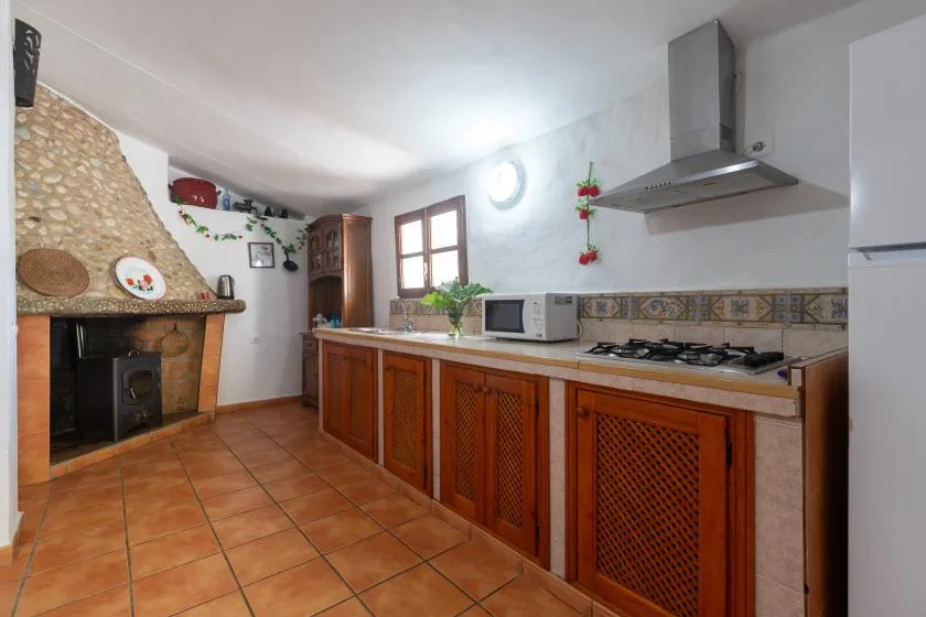 A rustic kitchen with a tiled floor, wooden cabinets, and a stone fireplace.
