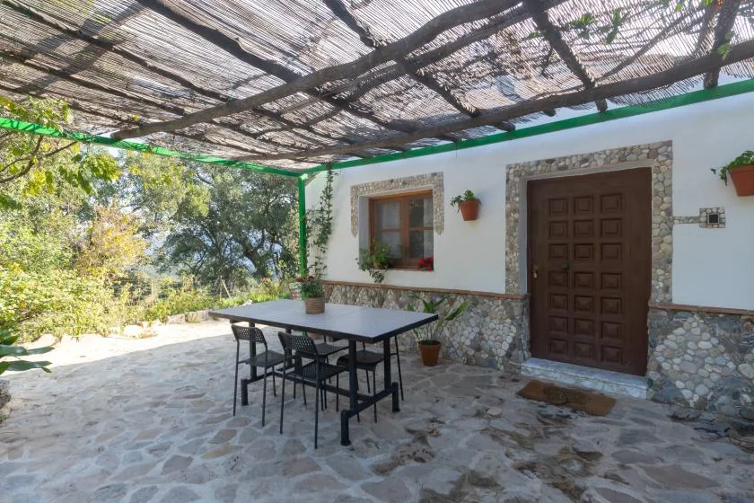 A stone-paved patio sits beneath a shaded canopy, with a table and chairs.