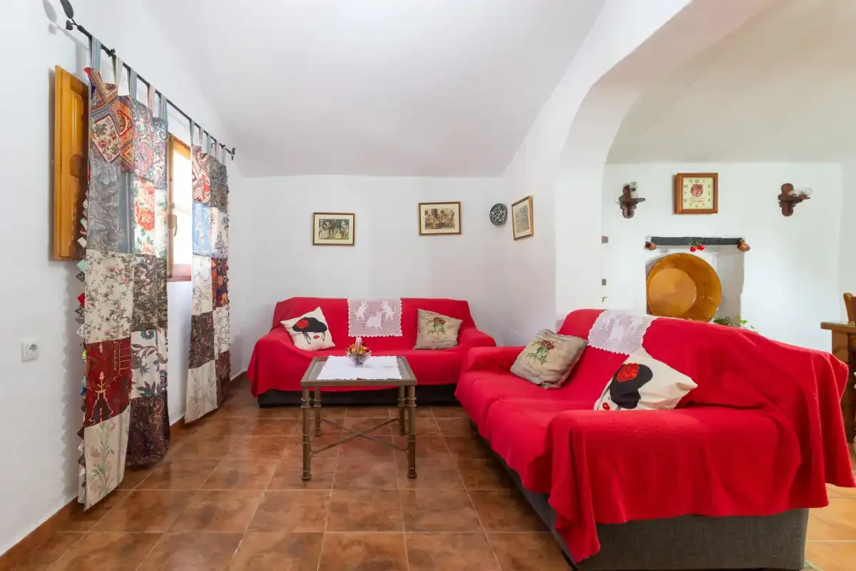 A living room with red-covered seating, a coffee table, and patterned curtains.