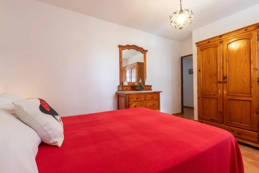 A bedroom with a red bedspread, wooden dresser, and matching wardrobe.