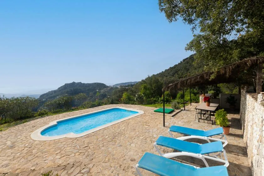 An outdoor swimming pool and seating area overlook green hills.