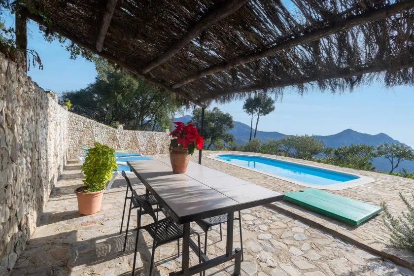 An outdoor dining area sits beside a swimming pool, with mountain views beyond.