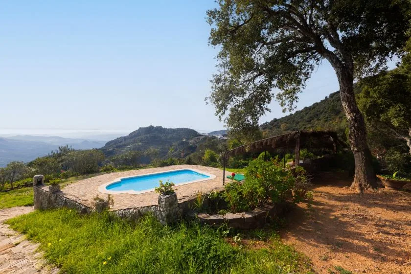 An outdoor swimming pool sits beside a garden, with hills visible in the distance.