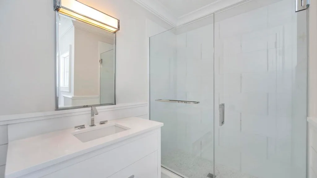 Un baño luminoso con un tocador blanco y una ducha de vidrio.