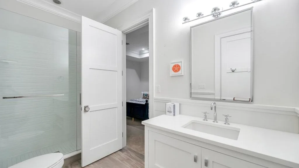 Un baño luminoso con un amplio lavabo y espejo junto a una ducha de vidrio.