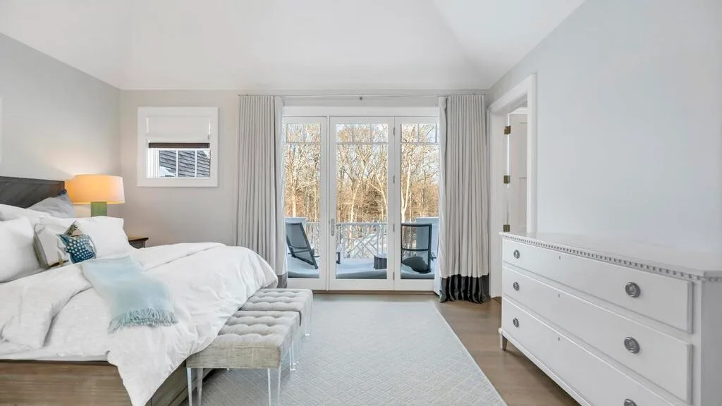 Un dormitorio luminoso con una cama frente a puertas de vidrio que dan a un balcón.