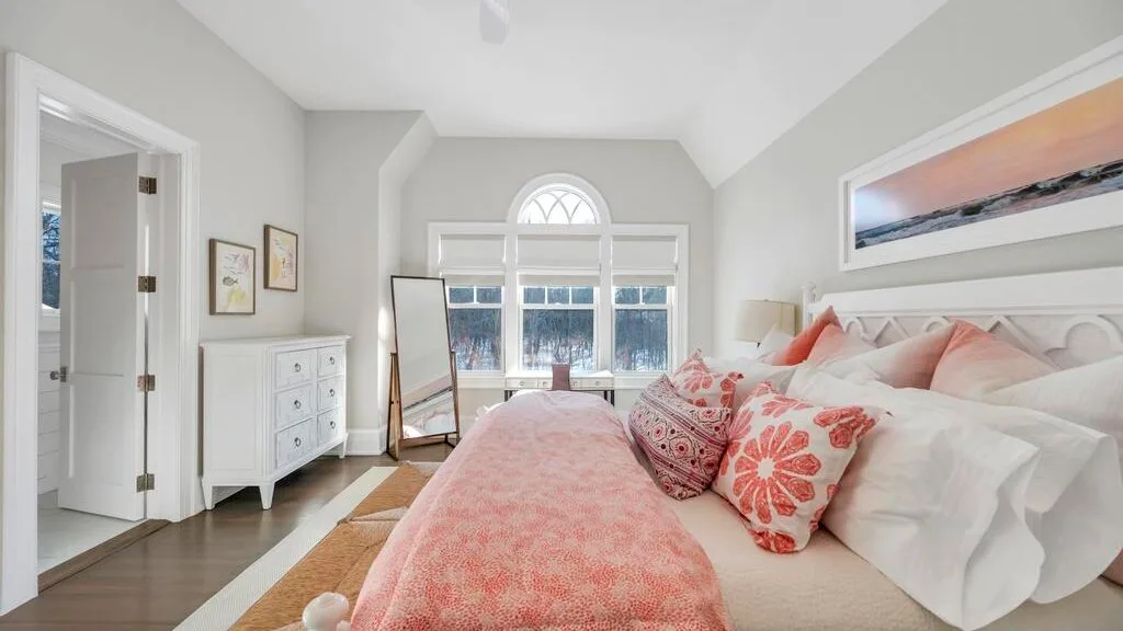 Un dormitorio luminoso con una cama grande vestida de blanco y coral.