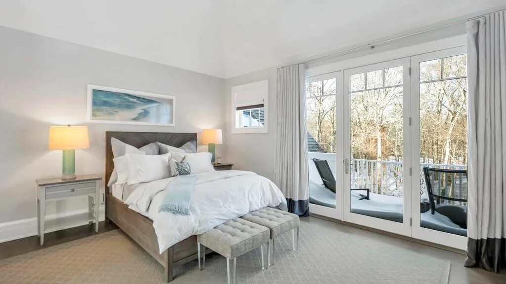 Un dormitorio luminoso con una cama junto a grandes ventanas que dan a un balcón.