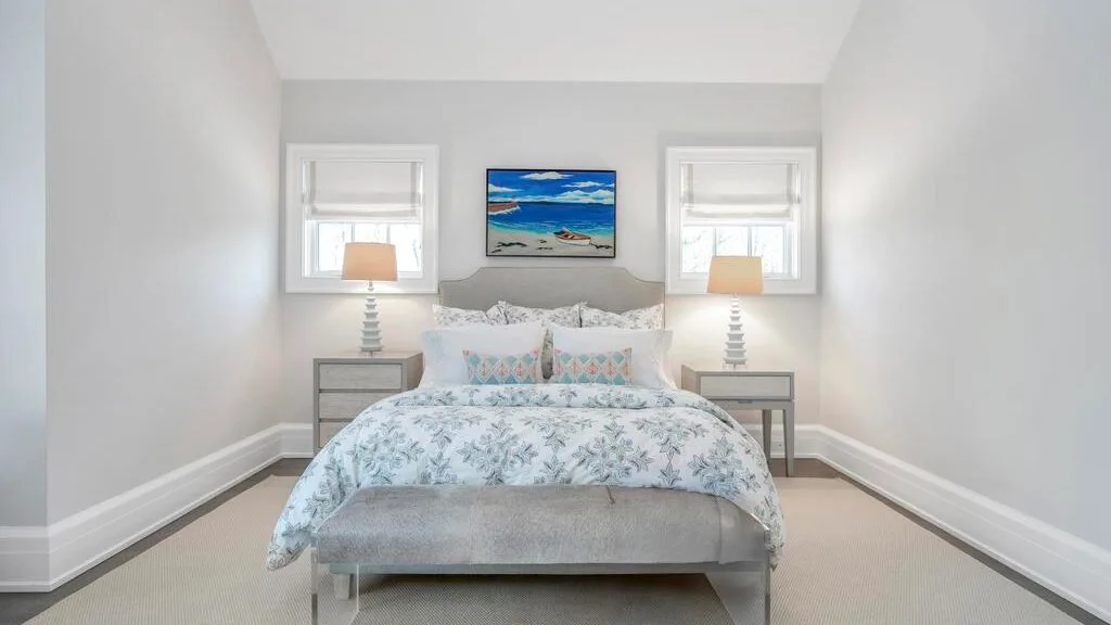 Un dormitorio luminoso con una cama bajo un colorido cuadro costero.