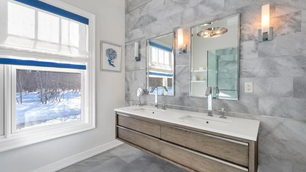 Un baño luminoso con un mueble largo, espejos y una vista nevada por la ventana.