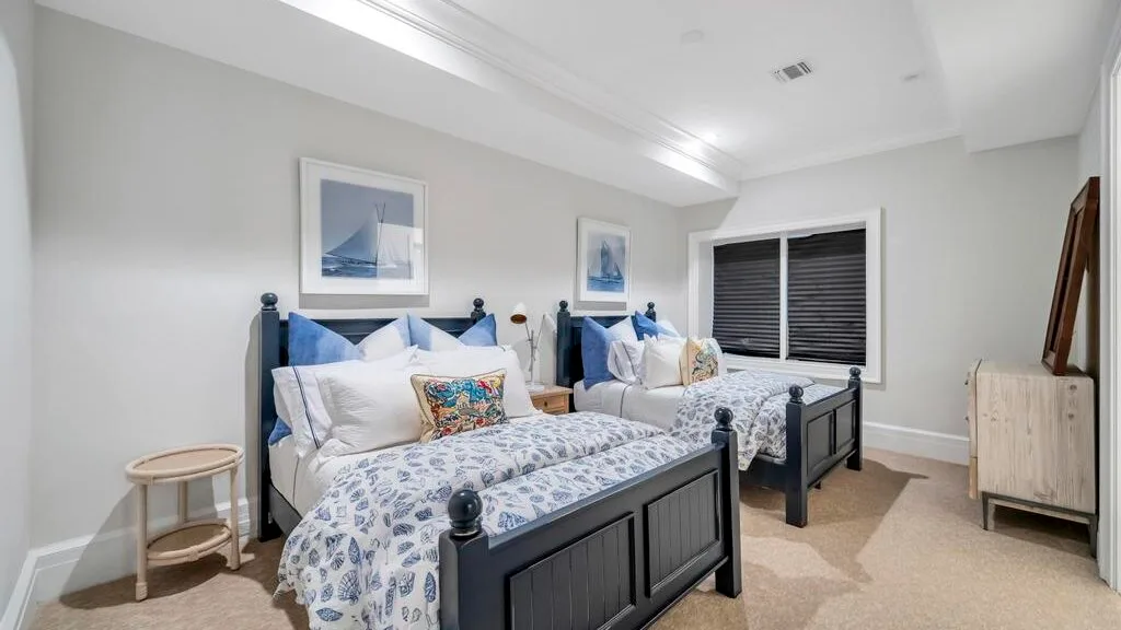 Un dormitorio luminoso con dos camas, ropa de cama estampada y una ventana con persianas oscuras.