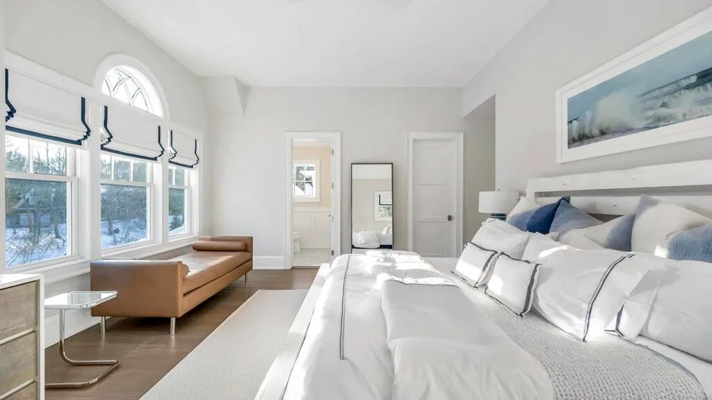 Un dormitorio luminoso con una cama grande, una zona de asientos marrón y ventanas altas.