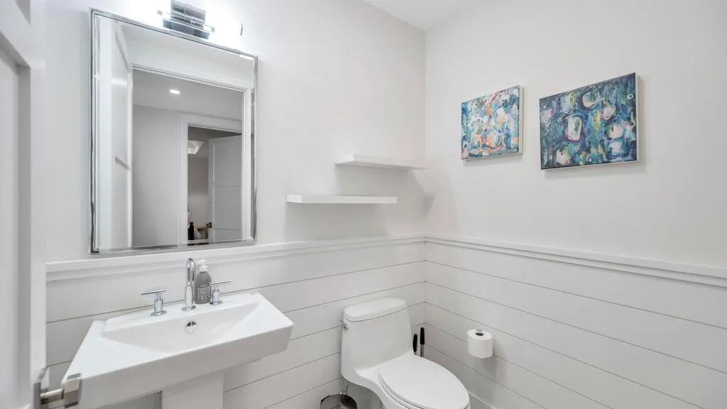Un baño luminoso con lavabo suspendido, inodoro y cuadros enmarcados.