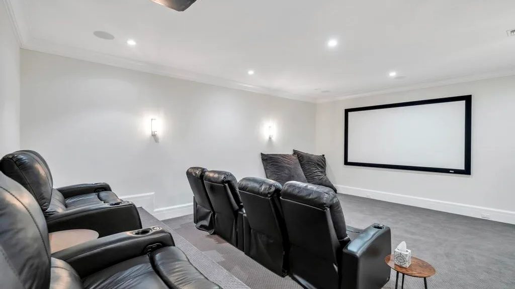 Una sala de cine en casa con filas de asientos reclinables oscuros frente a una pantalla grande.