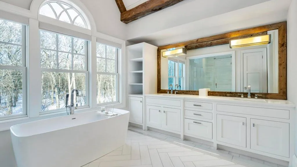 Un baño luminoso con una bañera exenta, grandes ventanas y un tocador largo.