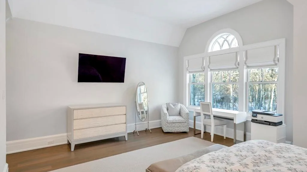 Un dormitorio luminoso con una cama, asientos y un escritorio junto a grandes ventanas.