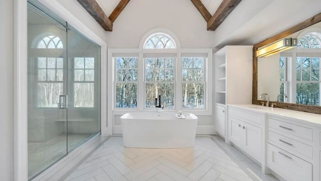 Un baño luminoso con bañera exenta, ducha de cristal y ventanas amplias.