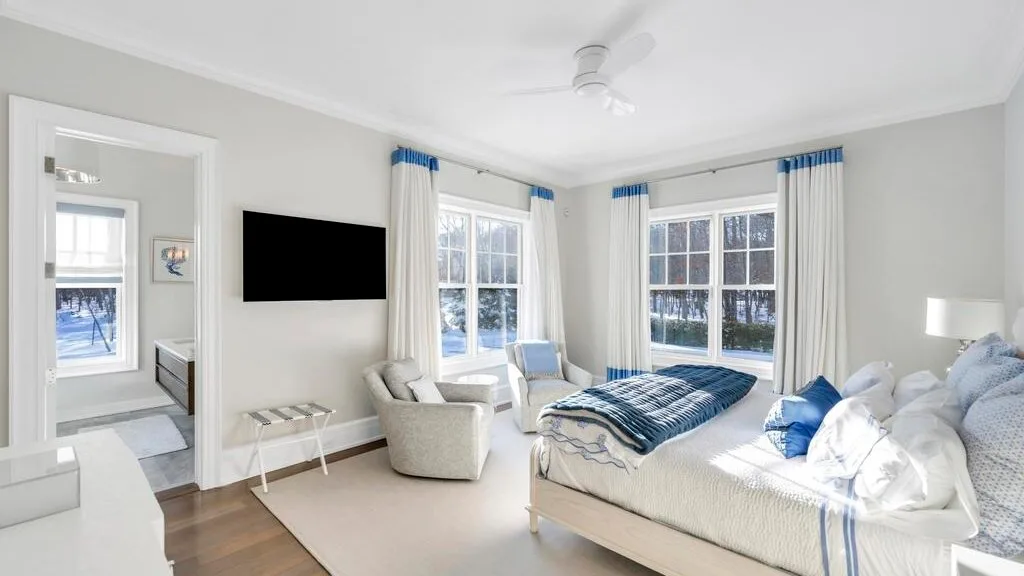 Un dormitorio luminoso con una cama, asientos y ventanas grandes.