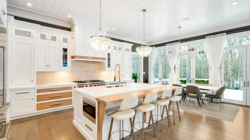 Una cocina y comedor luminosos con una isla larga y grandes ventanales.