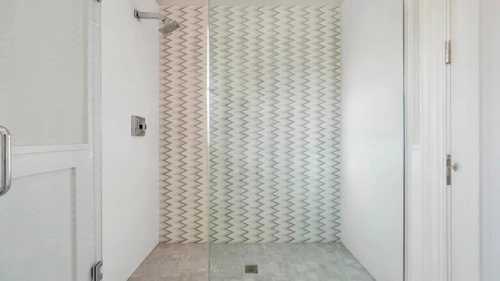 La zona de ducha de un baño tiene azulejos estampados y un desagüe en el suelo.