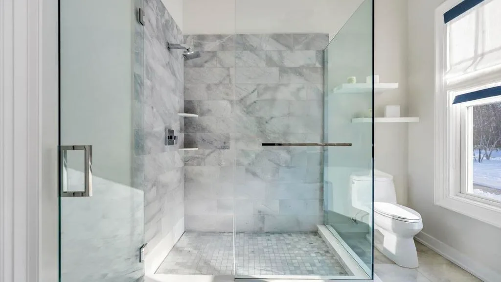 Un baño luminoso con una ducha de vidrio y una ventana.