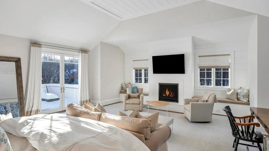 Sala luminosa con chimenea, asientos y ventanas que dan a un balcón.