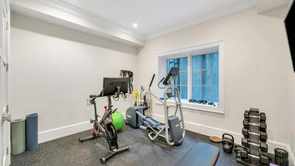 Un gimnasio en casa con máquinas de ejercicio y pesas junto a una ventana grande.