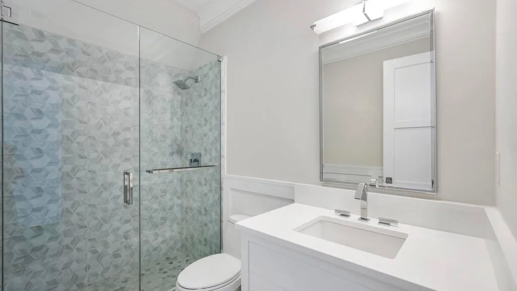 Un baño luminoso con una ducha de vidrio y un lavabo blanco.