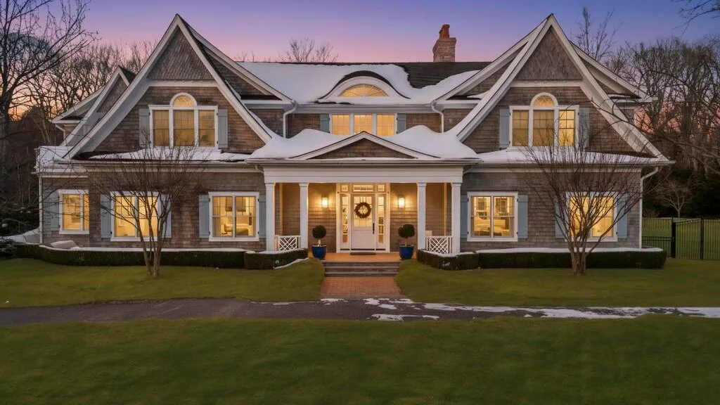 Una casa grande de dos plantas con frontones pronunciados y ventanas iluminadas al anochecer.