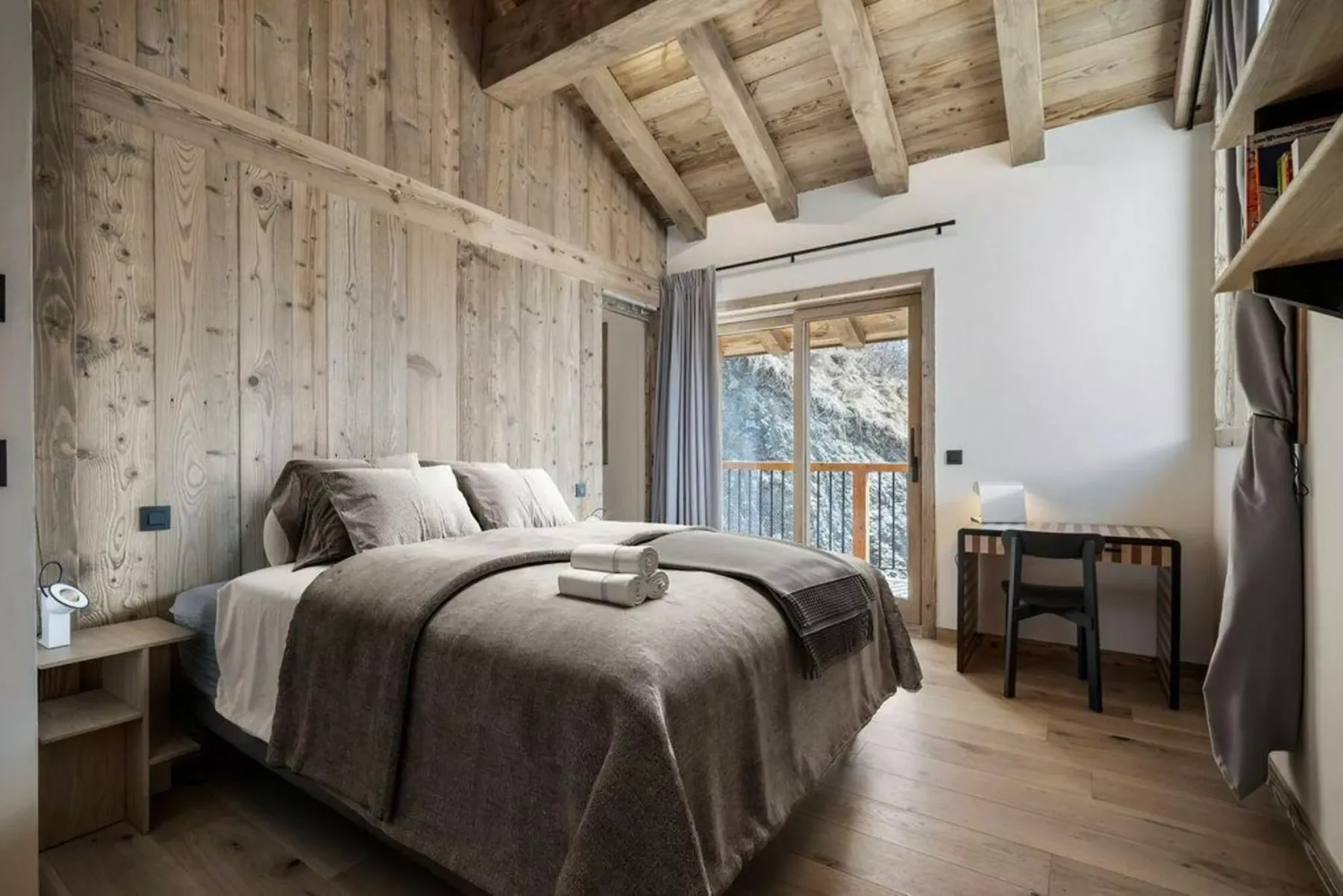 Un dormitorio con una cama, vigas vistas en el techo y una puerta al balcón.