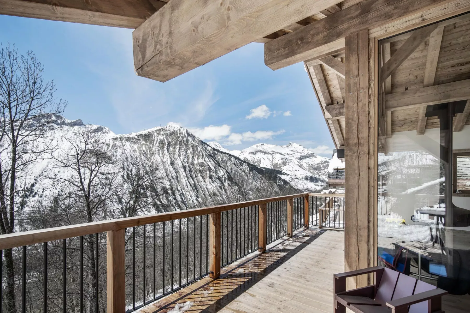 A wooden balcony overlooks snow-covered mountain peaks beneath a clear sky.