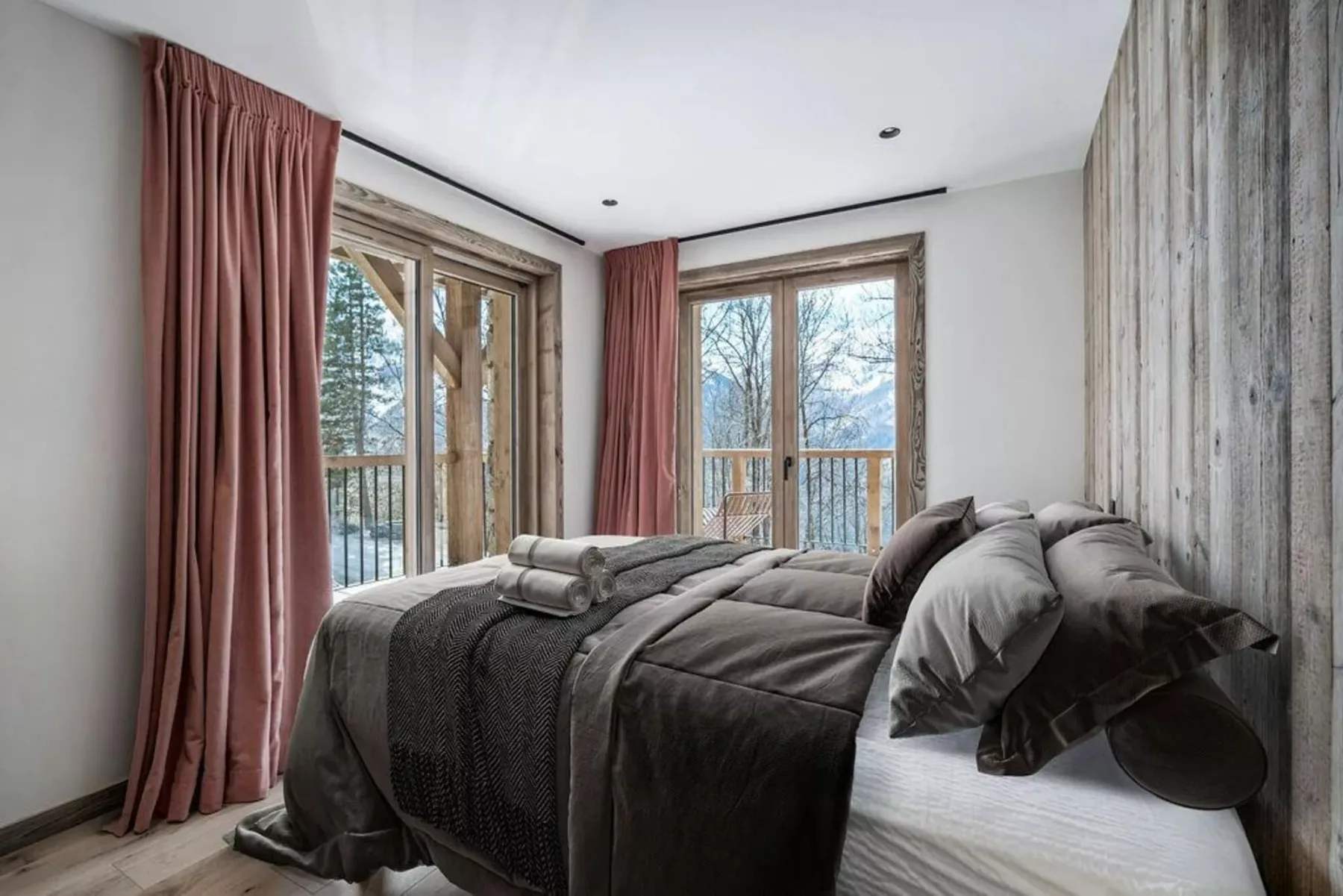 A bedroom with a bed beside tall windows and dusty rose curtains.