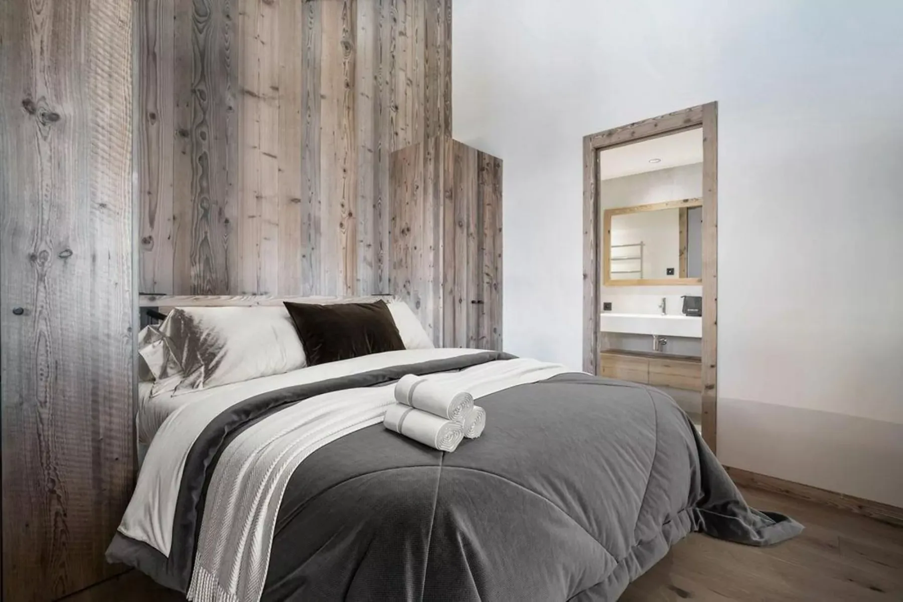 A bedroom with a neatly made bed and a wooden doorway opening onto a bathroom.