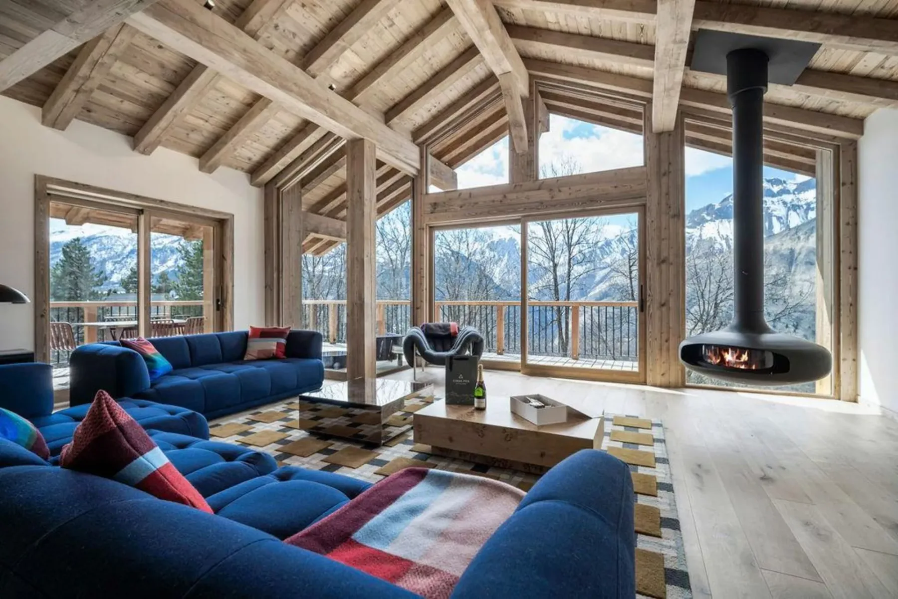 A bright living room with blue seating, a coffee table, and mountain views through large windows.