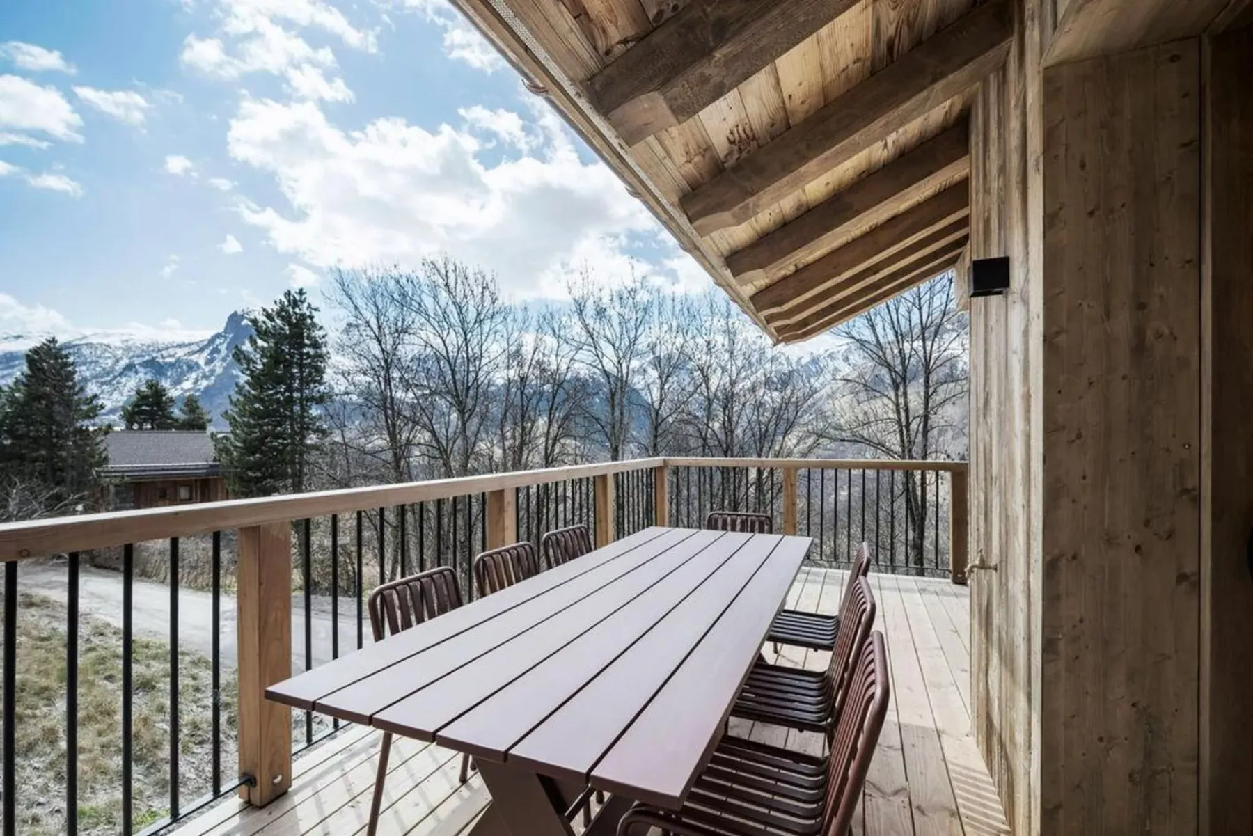 Una terraza de madera con una mesa de comedor exterior da a árboles y montañas lejanas.