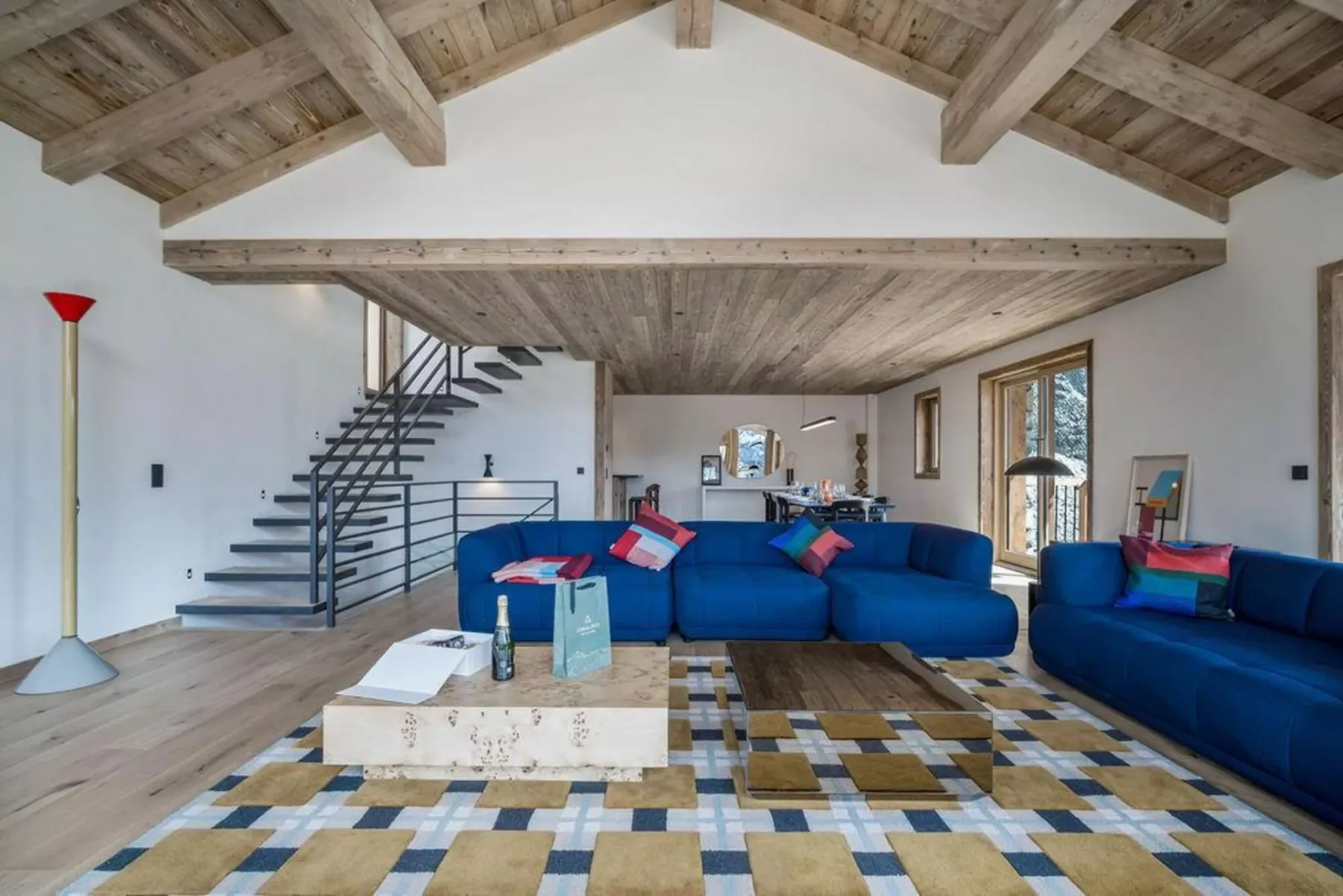 A bright living room with blue seating, a patterned rug, and an open staircase.