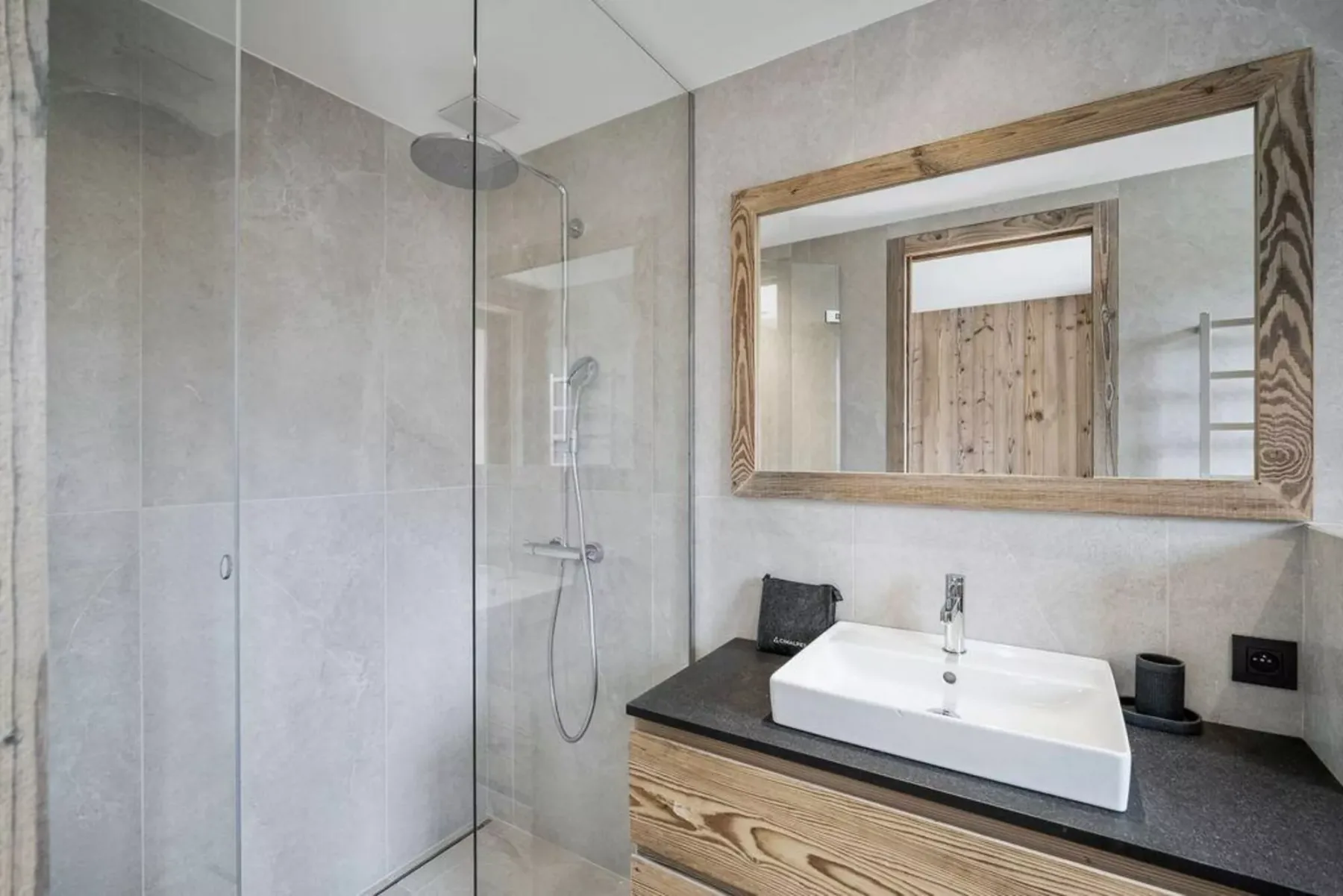 A bathroom with a glass shower and a sink beneath a framed mirror.